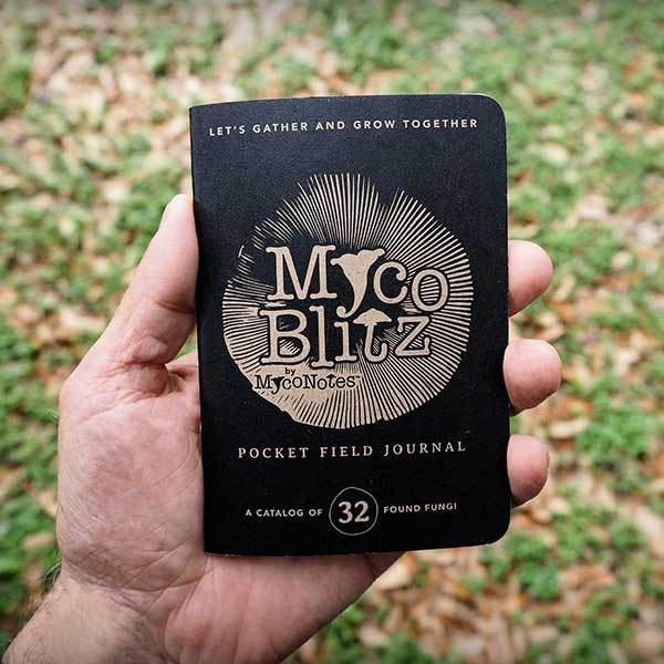 Hand holding a Myco Blitz pocket field journal against a natural background